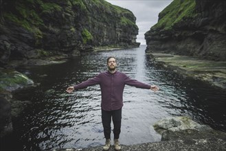 Denmark, Faroe Islands, Gjgv, Man standing inn gorge with outstretched arms