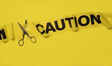 Studio shot of old fashioned scissors cutting caution tape on yellow background