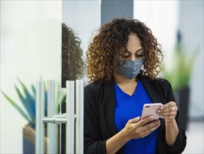 Businesswoman wearing face mask using smart phone in office