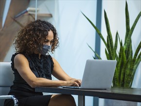 Businesswoman wearing face mask working on laptop at desk in office