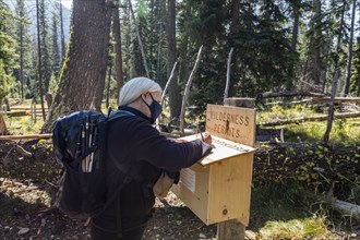 Senior woman in protective mask signing wilderness permit before hiking