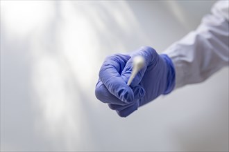 Gloved hand holds sterile swab for COVID testing