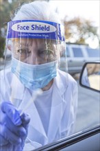 Female medical staff in protective clothing approaching car with coronavirus swab test