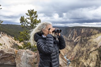 Senior woman looking through binoculars while standing above Grand Canyon in Yellowstone National Park