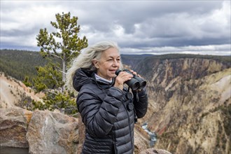 Senior woman holding binoculars while standing above Grand Canyon in Yellowstone National Park