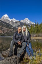 Outdoor portrait of senior couple sitting on rock by Taggart Lake in Grand Teton National Park
