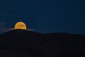 Full moon rising over mountains at night