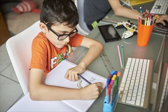 Boys (8-9) writing in notebook while learning at home during Covid-19 lockdown