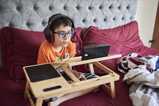 Boy (8-9) gaming on tablet while sitting in bed during weekend