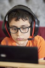 Boy (8-9) gaming on tablet while sitting in bed during weekend