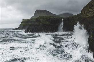 Coastline with Mulafossur Waterfall falling into Atlantic Ocean in stormy day