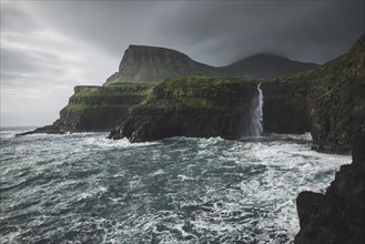Coastline with Mulafossur Waterfall falling into Atlantic Ocean in stormy day