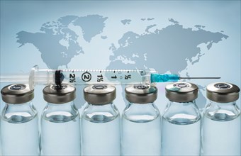 Row of Covid-19 vaccine vials and syringe with world map in background