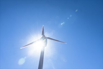Low angle view of wind turbine against blue sky and sun