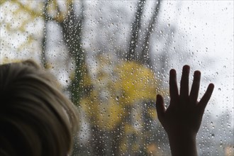 Close-up of boy (6-7) looking through window on rainy day