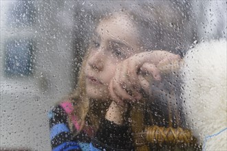 Close-up of girl (8-9) looking through window on rainy day