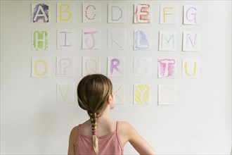 Rear view of girl (8-9) looking at alphabet on wall