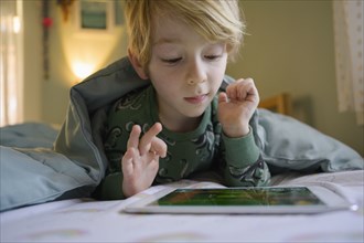 Boy (6-7) on bed using digital tablet