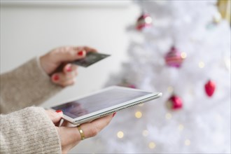 Hands holding tablet and credit card next to Christmas tree