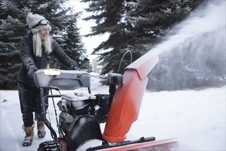 Senior woman clearing snow using snowblower