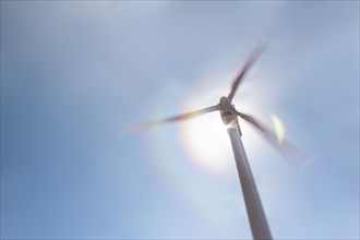 Low angle view of wind turbine against blue sky and sun