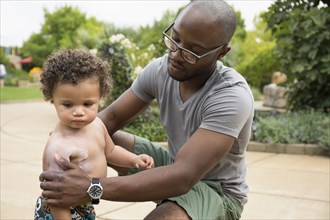 Father putting sunscreen on toddler son in park