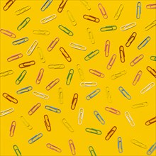 Multi colored paper clips scattered against yellow background