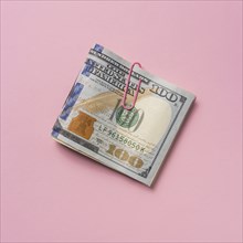 Folded one hundred dollar bill with paper clip on pink background