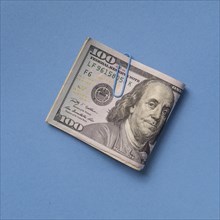 Folded one hundred dollar bill with paper clip on blue background