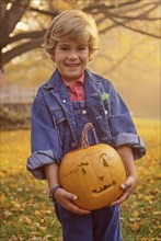 Portrait of smiling boy (4-5) holding carved Halloween pumpkin in field
