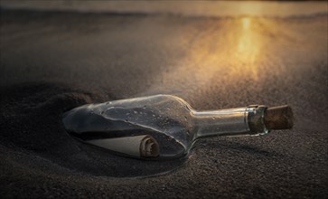 Glass bottle with message inside on beach at sunset