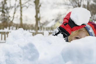Boy (6-7) hiding behind pile of snow and holding snowball