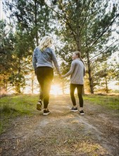 Rear view of mother and daughter holding hands and walking in landscape at sunset