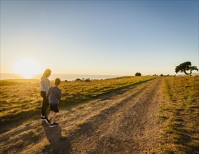 Rear view of mother and son walking in landscape at sunset