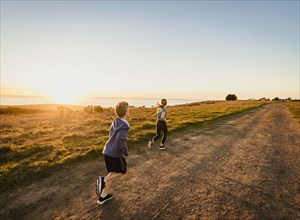 Rear view of boy and girl running on footpath in landscape at sunset