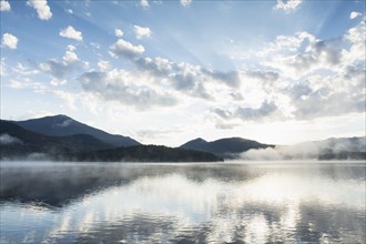 Mountains and clouds reflected in calm Lake Placid at sunrise
