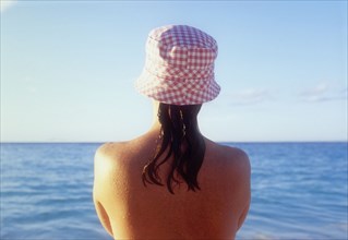 Rear view of woman in sunhat looking at sea