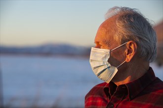 Outdoor portrait of senior man wearing COVID protective mask in sunlight