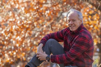 Outdoor portrait of senior man sitting near autumn tree