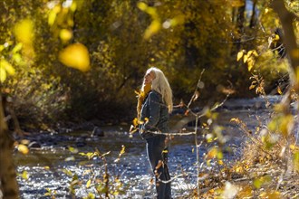 Senior woman standing in sunlight by river in autumn