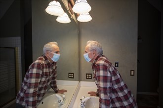Senior man wearing protective mask looking in bathroom mirror