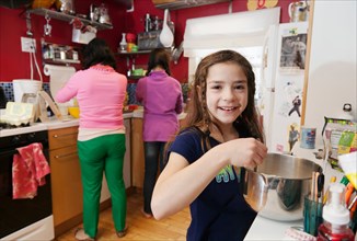 Girl in kitchen with mother and sister in background