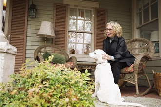 Senior woman sitting on porch rocking chair with dog