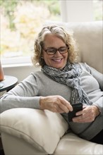 Relaxed senior woman sitting on sofa using mobile phone