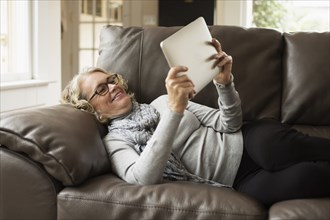 Senior woman reclining on sofa looking at digital tablet