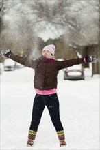Teenage girl throwing powdered snow mid air in street