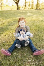 Portrait of girl and baby brother on grass in park