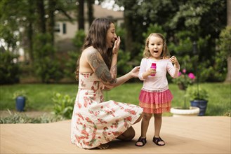 Mother and toddler daughter blowing bubbles in garden