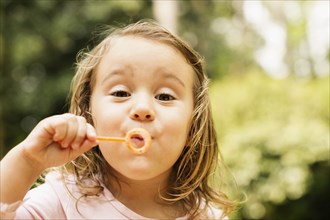 Close up portrait of female toddler blowing bubbles in garden