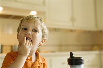 Male toddler eating with hands in kitchen